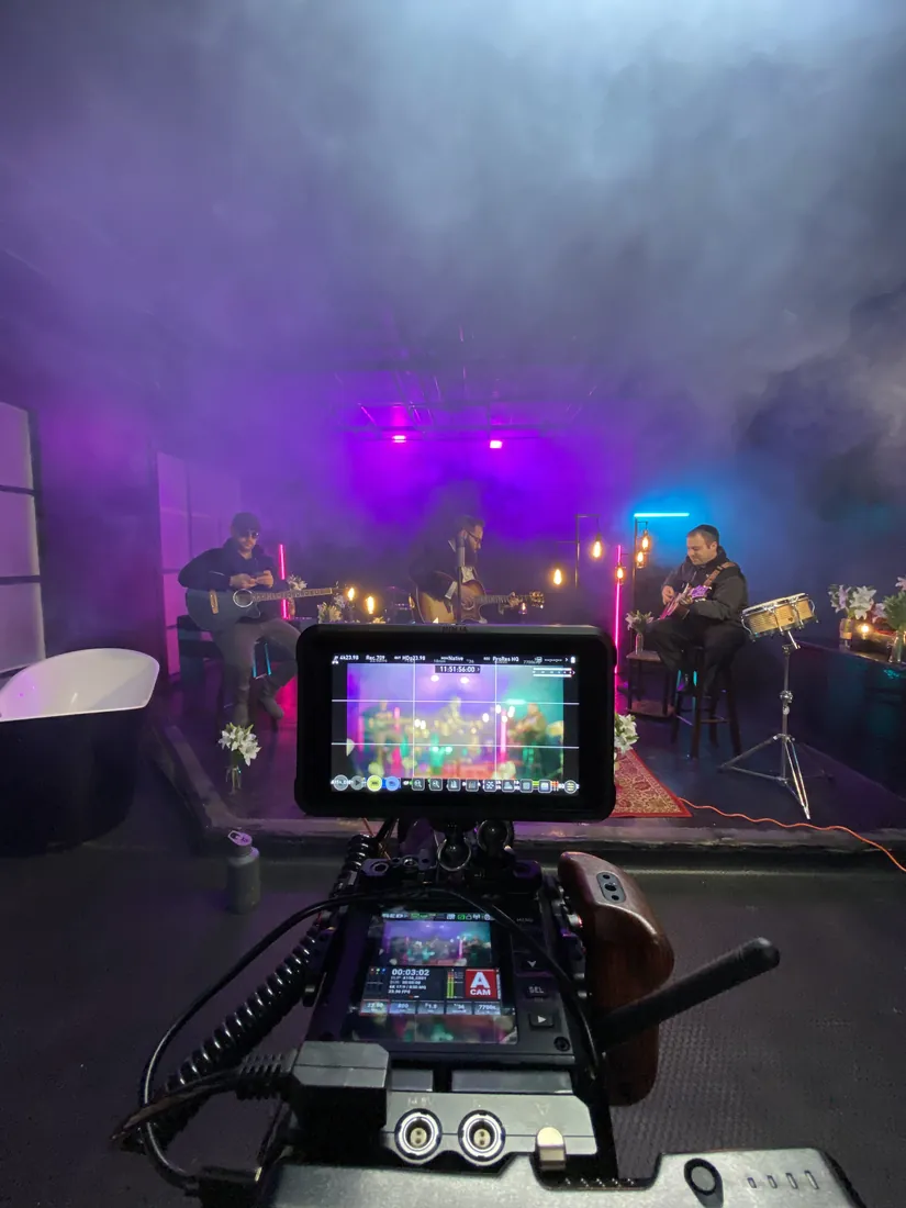 A camera monitor showing a band performing on a purple, fog-filled set.