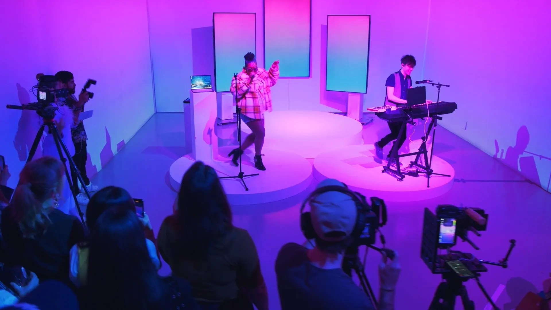Filming a live performance on a pink-lit stage in front of a crowd.
