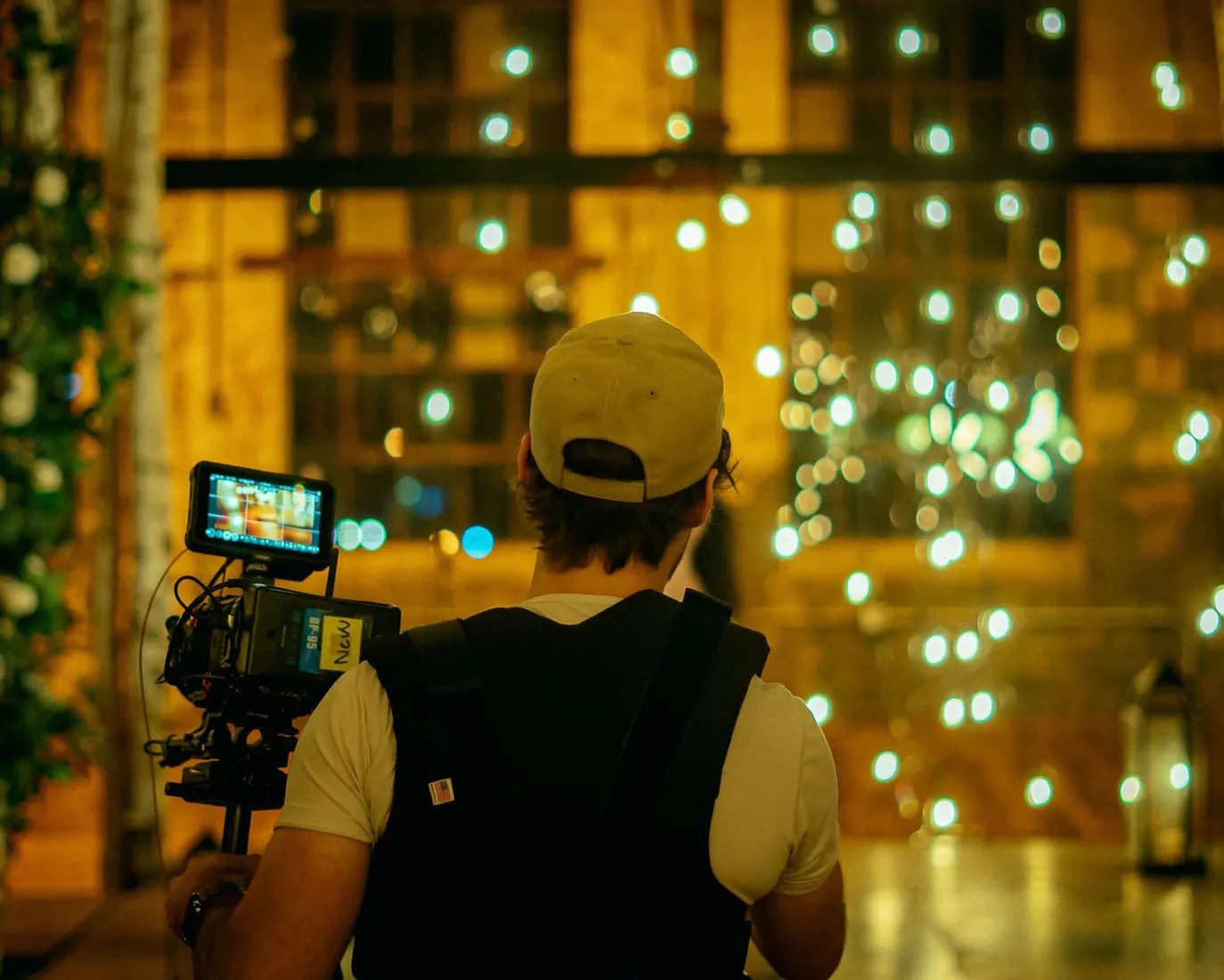 A camera operator filming in a room full of warm string lights.